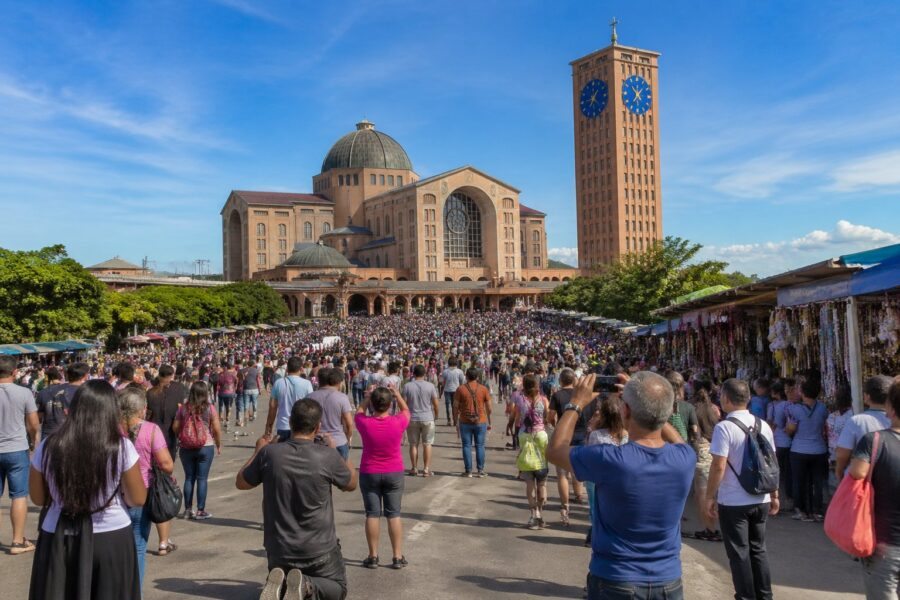 Vista da Basílica de Aparecida com fiéis e turistas reunidos em frente, barracas de artesanato ao redor e céu azul ao fundo.