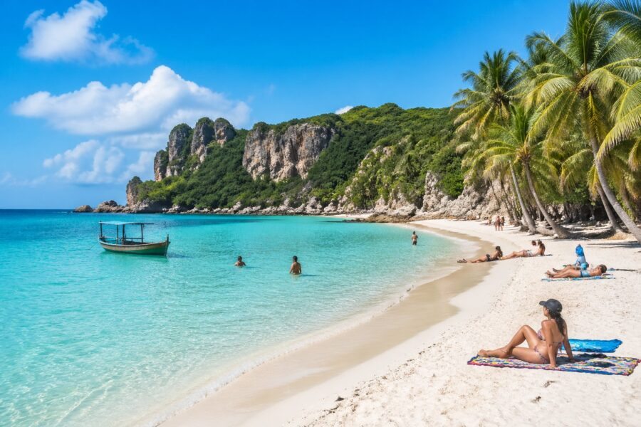Praia de Lagoinha com água cristalina, areia branca, coqueiros e pessoas aproveitando o mar e o sol.