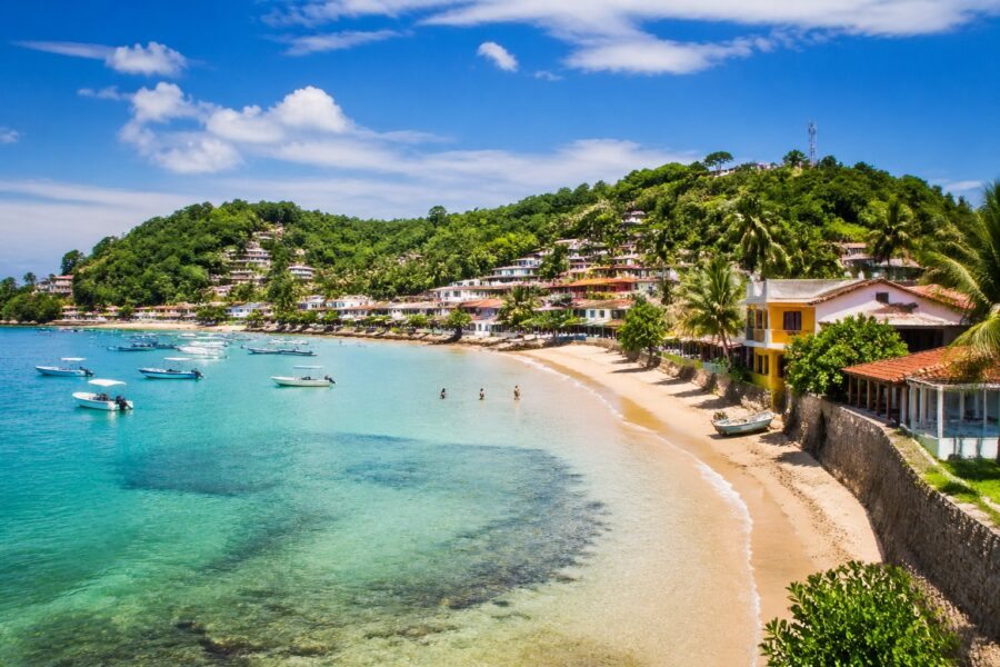 Vista panorâmica da costa de Morro de São Paulo com praias de areia dourada, águas turquesas, vegetação tropical e casas coloridas ao fundo.